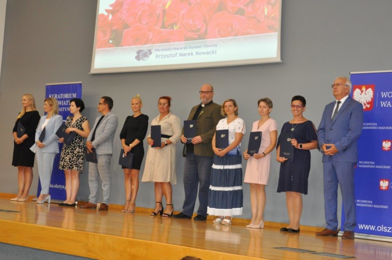 5 Warmińsko-Mazurski Kurator Oświaty wraz z nauczycielami, którzy otrzymali akty nadania stopnia awansu zawodowego nauczyciela dyplomowanego stoją na scenie