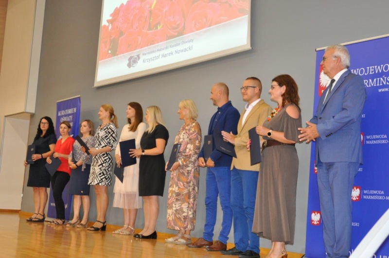 6 Warmińsko-Mazurski Kurator Oświaty wraz z nauczycielami, którzy otrzymali akty nadania stopnia awansu zawodowego nauczyciela dyplomowanego stoją na scenie